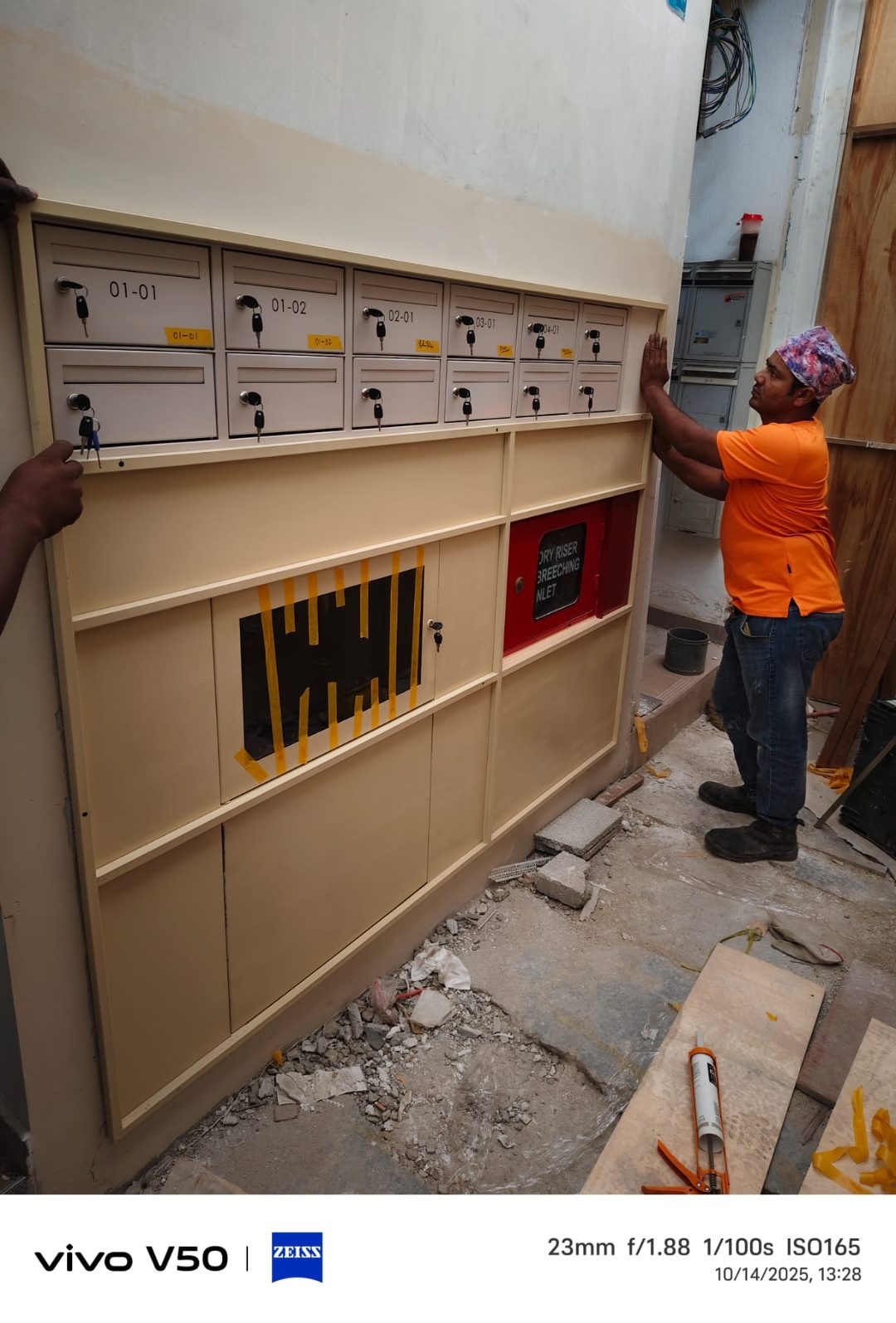 Wide front view of the Jalan Penhas mailbox installation with a worker fitting a slot panel in the lower row