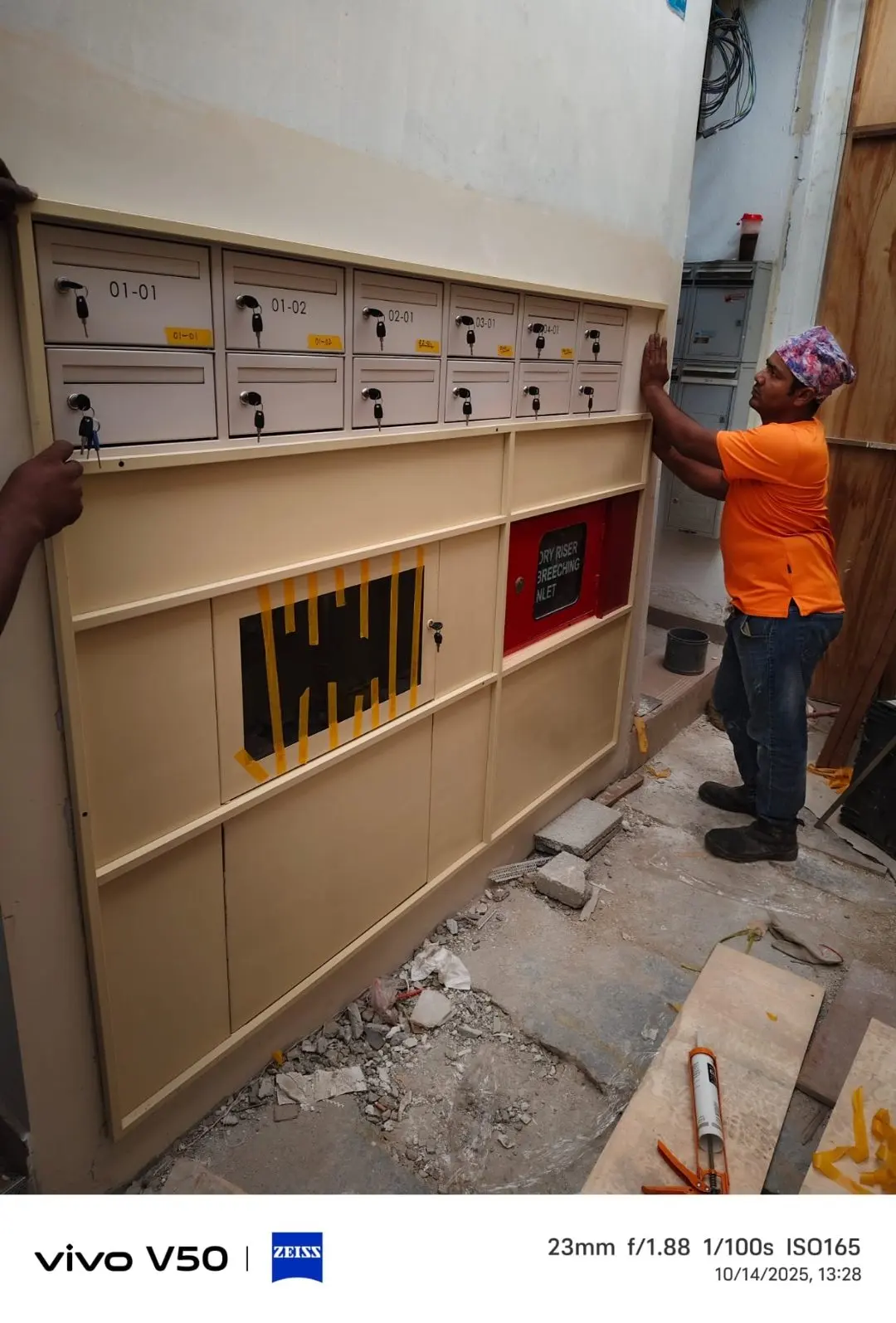 Wide front view of the Jalan Penhas mailbox installation with a worker fitting a slot panel in the lower row
