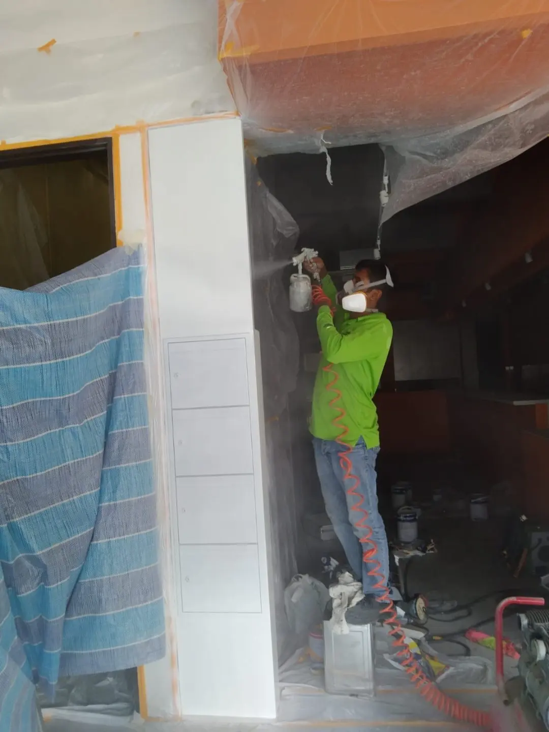 Painter applying paint to the entrance door surround at Outram Road with masking sheet and spray equipment in place