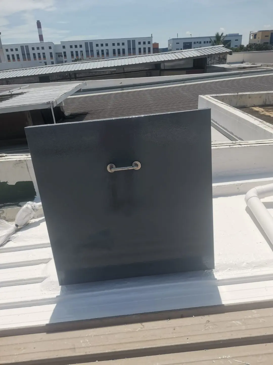 Closed roof access panel on the metal-deck roof at Tuas View with stainless pull handle