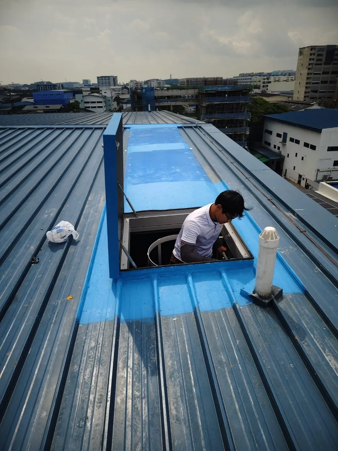 Roof-level view of the open access hatch at Wan Lee with worker emerging onto the metal-deck roof