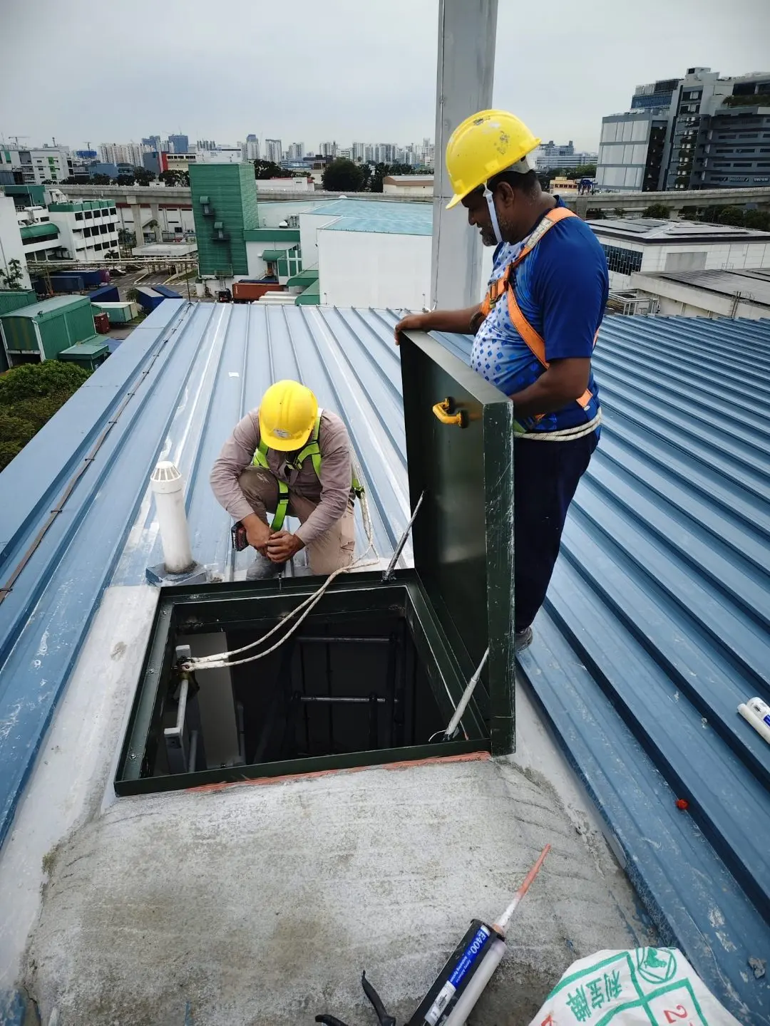 Workers fitting the roof access hatch frame onto the metal-deck roof at Wan Lee