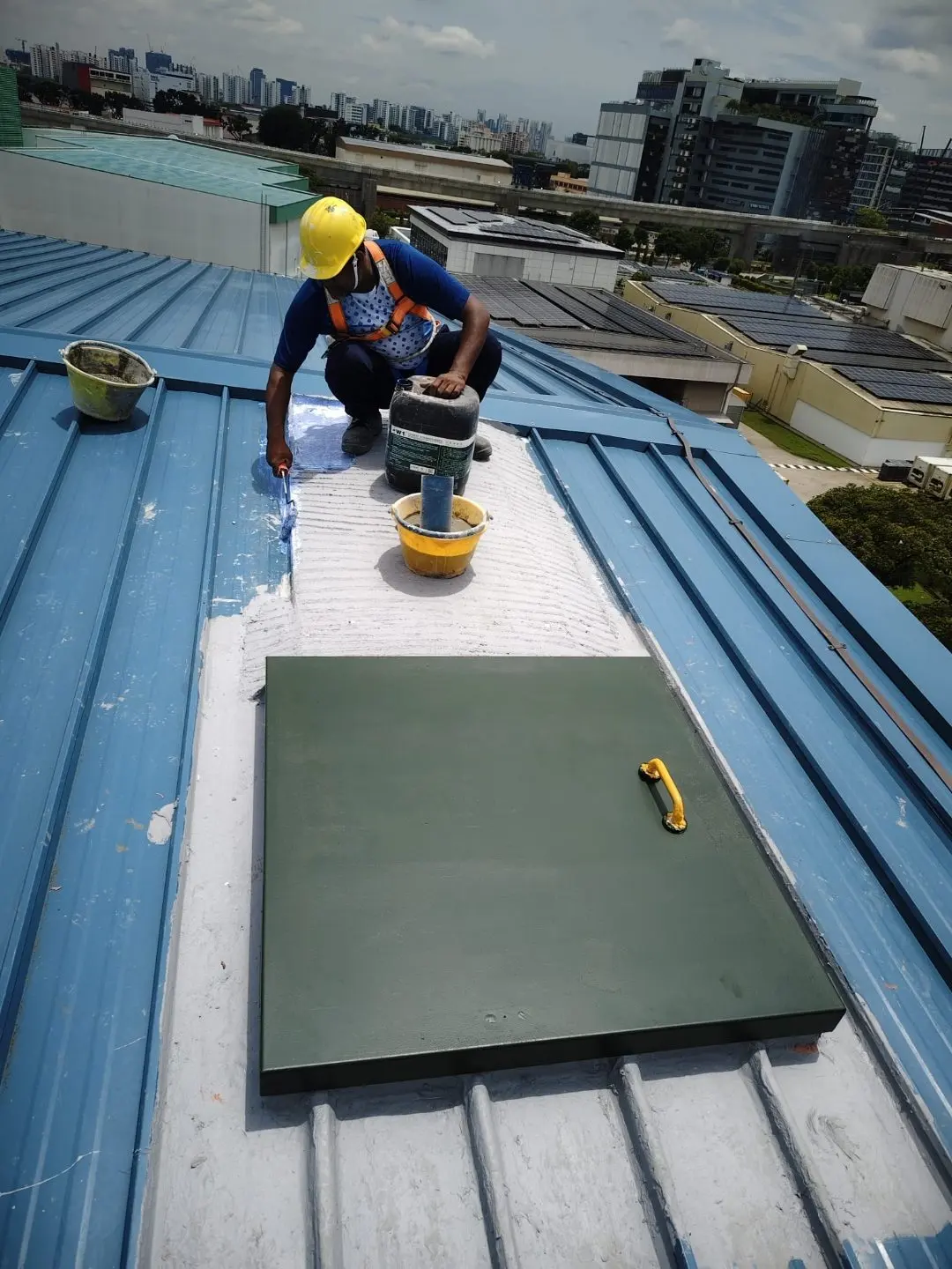 Worker preparing the roof access panel on the metal-deck roof at Wan Lee with grinding and fit-up tools